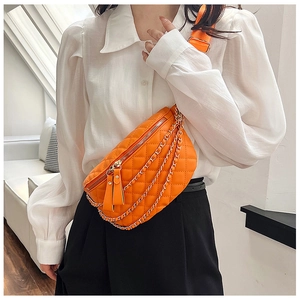 Close-up of orange quilted fanny pack with gold chains and fringe detail on model