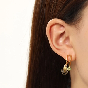 Detail of gold U-shaped earrings with green floral and fan pendants on a model