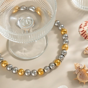 Elegant two-tone gold and silver beaded necklace on beach-themed aesthetic background
