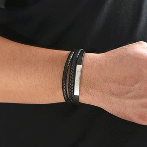 Detail of multi-strand braided black leather bracelet with rectangular silver metal plate
