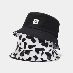 Reversible bucket hat featuring cow print pattern and black fabric with smiley face patch