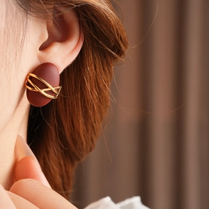 Detail of a dark red oval earring with golden cross patterns worn on a model's ear