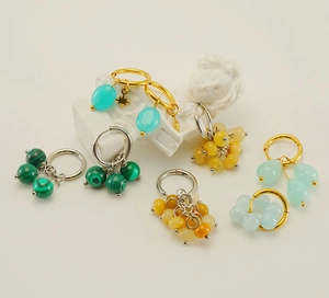 Close-up of 18k gold hoop earrings with malachite and natural stone charms on bust
