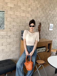 Outdoor summer outfit with cream pleated top, blue jeans, and orange woven bucket bag