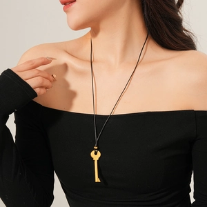 Gros plan d'un pendentif clé dorée sur un long collier en cuir noir porté par un mannequin