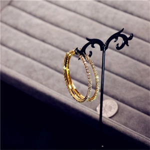Close-up of gold oversized crystal hoop earrings with rhinestones on a black vintage stand