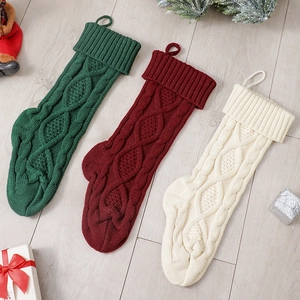 Three cable knit Christmas stockings in red green and cream on wooden floor decor