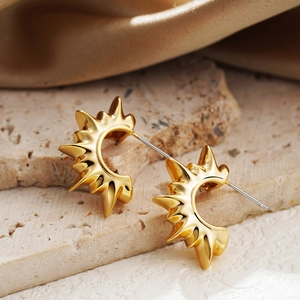 Exaggerated 18K gold sunburst C-shaped earrings on light stone and silk background