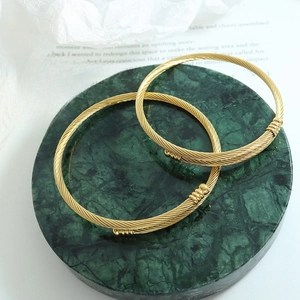 Minimalist gold spiral textured stainless steel open bangles on green marble tray