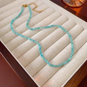 Gros plan du collier de perles géométriques bleu clair avec fermoir doré sur velours