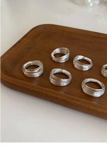 Detailed macro view of minimalist multi-layered silver geometric rings on wooden tray