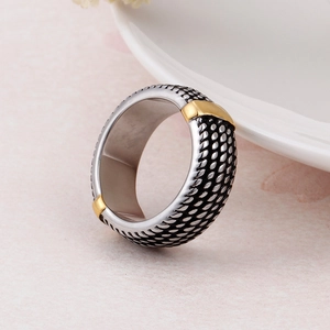 Close-up of wide stainless steel ring featuring black woven texture and gold accents