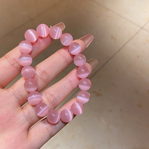 Close-up of pink cat eye stone beaded bracelet with glossy sheen on a person's hand