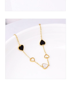 Detailed close-up of a gold heart bracelet with black enamel and white mother of pearl charms