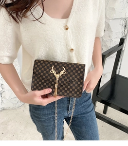Detail of dark brown flap bag with geometric print, deer head hardware and gold tassel