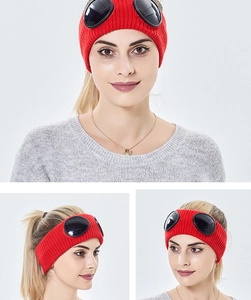 Detail of red knitted headband with black goggle lenses on a light gray background