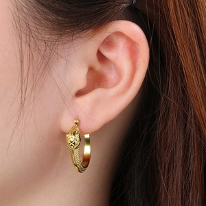 Macro view of golden snake hoop earrings featuring 3D scale texture on a model's ear