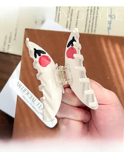Detail of cream butterfly hair claw clip with red cherry pattern held by hand