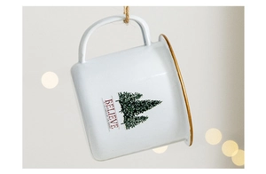 Detail of white enamel Christmas mug with green pine tree and Believe text in festive bokeh