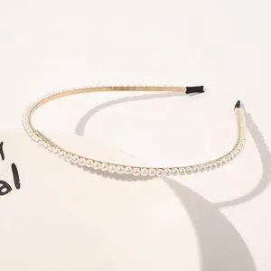 Macro detail of thin gold headband with white pearls on a minimalist white tray