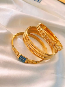 Detail view of four gold stackable bracelets with blue zircons on white silk background