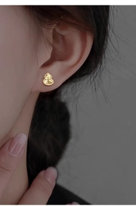 Detail of gold gourd-shaped stud earring with honeycomb texture on a female ear model