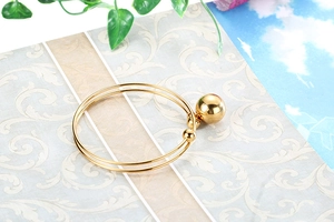 Detailed view of a gold double-layer bangle with a polished mirror ball pendant on a table