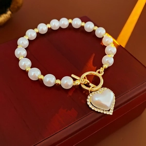 Dettaglio ciondolo a cuore con zirconi e perle su bracciale dorato con chiusura OT