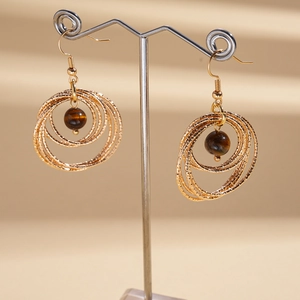 Detail of layered gold circles with a brown tiger eye stone on a metal hook earring
