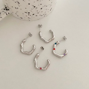 Set of wavy silver stainless steel earrings with colorful gemstone inlays on beige background