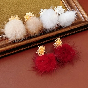 Close-up of plush pom-pom earrings in beige, white, and red with gold zircon studs