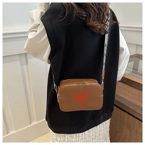 Side view of brown leather crossbody bag with red heart pattern and geometric strap
