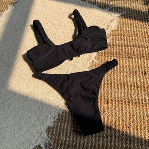 Detail of black two-piece bikini with ruched shoulder straps and shimmering fabric texture