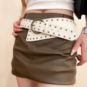 Close-up of white leather belt featuring brass studs and a large round metal buckle