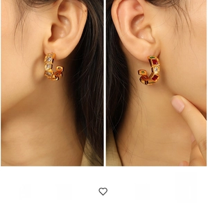 Detailed view of gold plated C-shaped earrings with vibrant inlaid gemstones on ear