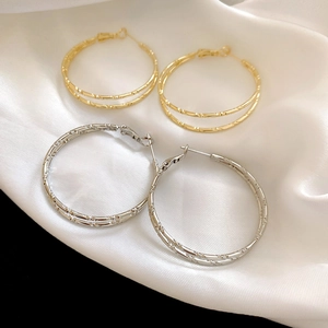 Macro shot of gold and silver double-layered bamboo hoop earrings on white silk fabric