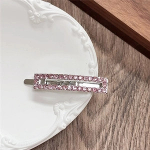 Detailed view of pink rhinestone geometric metal hair clip on a white ceramic tray