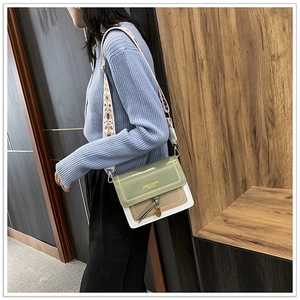 Detail of color-block crossbody bag with wide ethnic-style strap and gold logo text