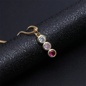 Macro shot of gold necklace with three-stone vertical pendant on black leather