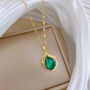 Close-up of golden necklace with green pear-shaped gemstone pendant on jewelry box