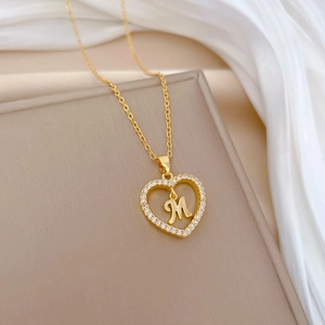 Gold heart necklace with letter M and sparkling crystals on soft white silk background