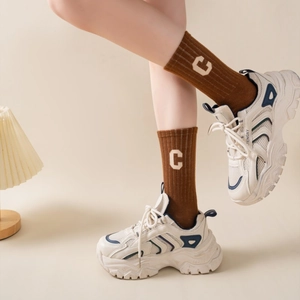 Close-up of beige sneakers and brown ribbed crew socks with white letter C embroidery