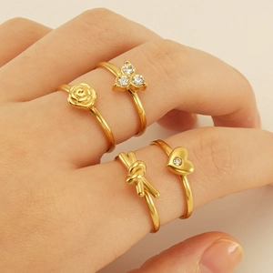 Close-up of four gold stacking rings featuring rose, heart, knot, and zircon details
