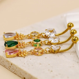 Détail macro de piercings de nombril dorés avec zircons roses, verts et transparents