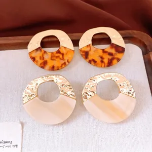 Hammered gold and tortoiseshell resin hoop earrings on a luxury linen wood tray