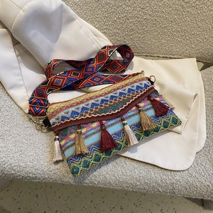 Detail of bohemian woven square bag featuring multi-color tassels and wide patterned strap