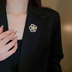 Détail de la broche camélia dorée avec perle et strass sur le revers d'une veste noire