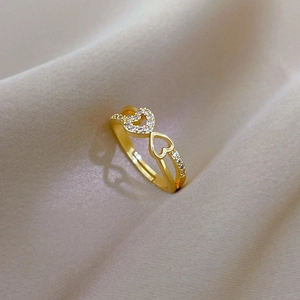 Close-up of golden heart ring with white zircon stones on champagne fabric background