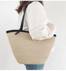 Handwoven beige straw tote bag with black strap worn by a model in a side view