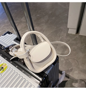 Mini sac à main en cuir crème posé sur une valise argentée dans une scène de voyage